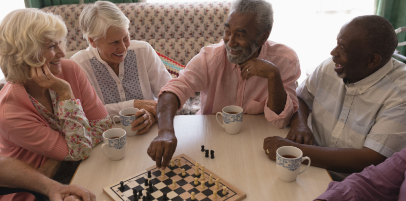 Gruppe älterer Menschen spielt Schach und trinkt Kaffee.